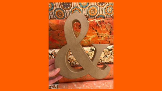 Photo of an ampersand symbol being held by a hand against an orange background.